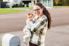 Mum With Young Baby Checking The Mailbox Smiling Together Outside