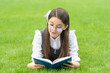 Leinwandbild Motiv Serious schoolgirl reading book lying on grass, reading. Teen girl reading outdoors