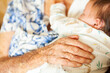 © Austockphoto - Old loving hands of great granny on sleepy newborn baby