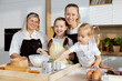 © ABCreative - Mom and eldest daughter looking at screen smiling. Preschooler daughter trying pour flour into bowl granny looking at younger grandchild smiling.