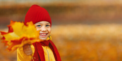 Portrait of a girl with a wide open smile holding red and yellow autumn leaves in her hand.