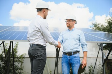 Workers shaking hands on a background of solar panels on solar power plant