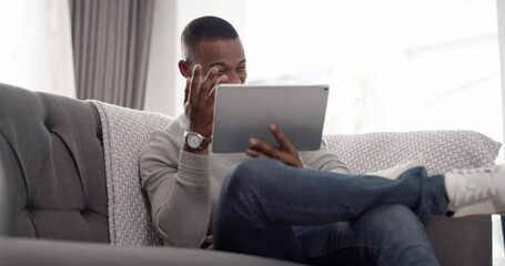 Fototapete - Trendy, funny and laughing man watching comedy video or social media meme content on a tablet on the sofa at home. A young and relaxed guy looking at or enjoying a film, movie or show online on couch