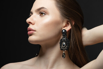 Beauty, fashion, style, jewelry and make-up concept. Beautiful and sexy looking brunette woman with fancy black earrings with gemstones studio portrait. Model looking aside the camera