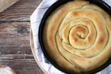 Traditional homemade savory pie with cheese on a rustic wooden table dusted with flour. Top view, a closeup. Tasty Balkanian pastry, Macedonian cuisine.