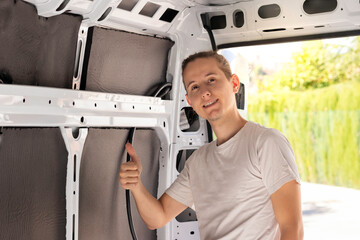 Young man looking to camera with thumbs up sign after making a great job isolating the camper van