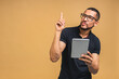 © denis_vermenko - Working on digital tablet. Portrait of happy smiling young African american black man holding digital tablet while standing isolated over beige background.
