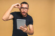 © denis_vermenko - Working on digital tablet. Portrait of shocked amazed surprised young African american black man holding digital tablet while standing isolated over beige background.