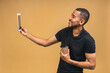 © denis_vermenko - Working on digital tablet. Portrait of happy smiling young African american black man holding digital tablet while standing isolated over beige background. Drinking coffee.