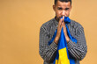 © denis_vermenko - Portrait of sad negative african american black guy holding ukrainian flag, isolated over beige background.