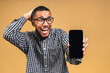 © denis_vermenko - Portrait of a smiling attractive african american black man holding blank screen mobile phone isolated over beige background.