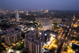 Fototapeta Londyn - aerial drone shot showing brightly lit orange streets with skyscrapers, towers housing homes offices and shopping complexes in between with the city skyline in the distance in Gurgaon Delhi India