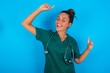 Photo of upbeat beautiful doctor woman wearing medical uniform over blue background has fun and dances carefree wear being in perfect mood makes movements. Spends free time on disco party