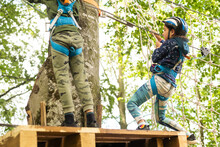 Little Girl Preschooler Wearing Full Climbing Harness Having Fun Time In The Rope Park Using Carabiner And Other Safety Equipment. Summer Camp Activity For Kids. Adventure Park In The Forest