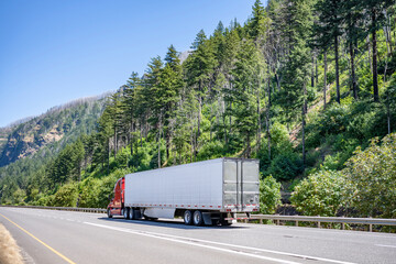 Bright red big rig industrial semi truck with refrigerator semi trailer transporting cargo running on the gorgeous highway road on Columbia River Gorge national reserve area