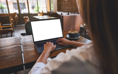 Wall Mural - mockup image of a woman using and typing on laptop computer with blank white desktop screen in cafe