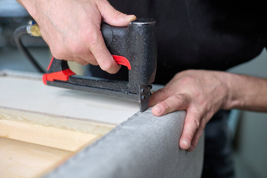 Worker qualitatively fixes the fabric with a pneumatic stapler on the body in the factory shop. Production of upholstered cabinet furniture.
