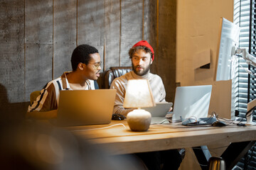 two men with different nationality working on computers, sitting together at cozy home office. conce