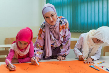 Wall Mural - Group of happy Muslim school kids with their teacher working on project together at classroom.