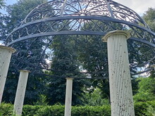 Bottom View While Relaxing On A Park Decorative Gazebo Surrounded By Tall Green Trees Under A Cloudy Blue Sky.
