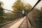Fototapeta  - Slender athletic young woman in the morning jogging on a suspension bridge in a mountain village.
