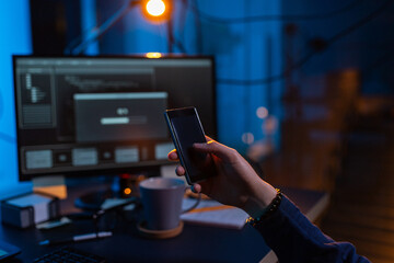 cybercrime, hacking and technology concept - close up of male hacker with smartphone using computer virus program for cyber attack in dark room