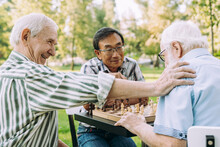 Group Of Senior Friends Playing Chess At The Park