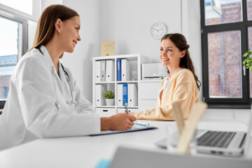 medicine, healthcare and people concept - female doctor with clipboard talking to smiling woman patient at hospital