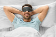© Syda Productions - people, bedtime and rest concept - happy smiling man in sleeping eye mask lying in bed, top view