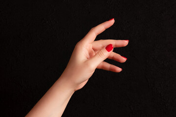 Wall Mural - Female hand with beautiful manicure - red nails on dark black background