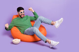 Fototapeta Panele - Full body photo of young latin man sit soft beanbag raise fists enjoy movie dressed stylish green look isolated on purple color background