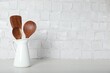 Set of wooden kitchen utensils in jug on table near white wall. Space for text
