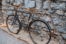 An Old Rusty Two-wheeled Bicycle Stands Against The Background Of A Stone Wall, Ancient Means Of Transportation.