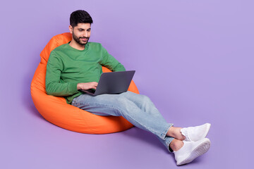 Wall Mural - Full body photo of young latin guy sitting coding new software entrepreneur wear stylish green garment isolated on purple color background