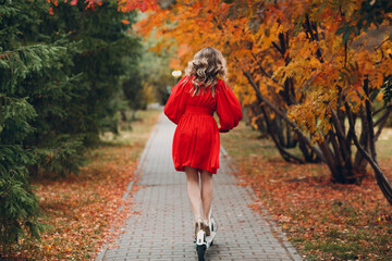 Wall Mural - Young woman with electric scooter in red dress at the autumn city park.