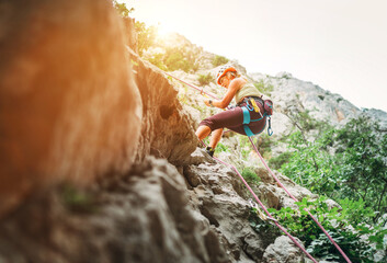 Active climber woman in protective helmet abseiling from cliff rock wall using rope with belay device and climbing harness. Active extreme sports time spending concept.