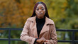 © Yuliia - Upset frustrated african american woman shows on watch, counting minutes, rushing. Portrait of beautiful afro girl standing in autumn park alone. Running out of time, hurry, to be late concept
