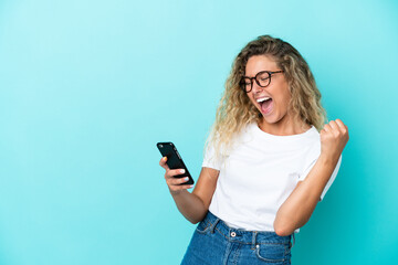 Wall Mural - Girl with curly hair isolated on blue background with phone in victory position