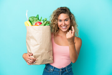 Wall Mural - Girl with curly hair holding a grocery shopping bag isolated on green background doing coming gesture