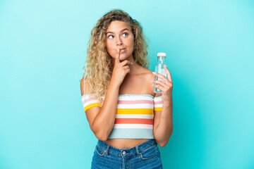 Wall Mural - Young blonde woman with a bottle of water isolated on blue background having doubts while looking up