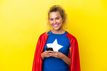 Wall Mural - Super Hero woman isolated on yellow background looking at the camera and smiling while using the mobile