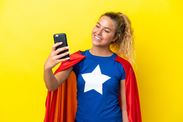 Wall Mural - Super Hero woman isolated on yellow background making a selfie with mobile phone