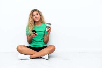 Wall Mural - Girl with curly hair sitting on the floor holding coffee to take away and a mobile while thinking something