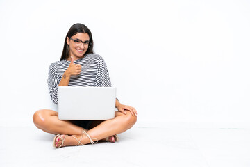 Young caucasian woman with a laptop sitting on the floor giving a thumbs up gesture