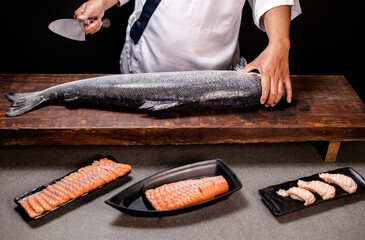 Chef's hand holding fresh piece of salmon.Closeup of chef hands preparing japanese food. Japanese chef making sushi at restaurant.Chef making traditional japanese sushi on wood board.