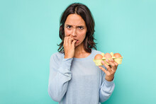 Young Hispanic Woman Holding Eggs Isolated On Blue Background Biting Fingernails, Nervous And Very Anxious.
