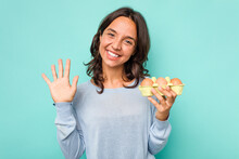 Young Hispanic Woman Holding Eggs Isolated On Blue Background Smiling Cheerful Showing Number Five With Fingers.