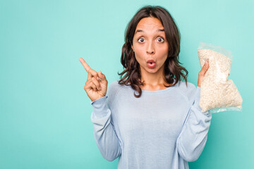 Wall Mural - Young hispanic woman holding a bag of oats isolated on blue background pointing to the side