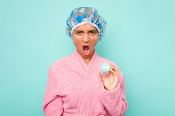 Wall Mural - Young hispanic woman holding bathtub ball isolated on blue background screaming very angry and aggressive.