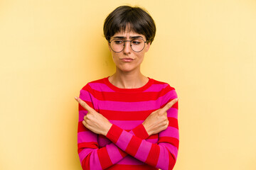 Young caucasian woman with a short hair cut isolated points sideways, is trying to choose between two options.